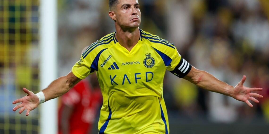Jogador de futebol comemorando gol com os braços abertos, vestindo uniforme amarelo e azul em campo de futebol, expressão intensa.