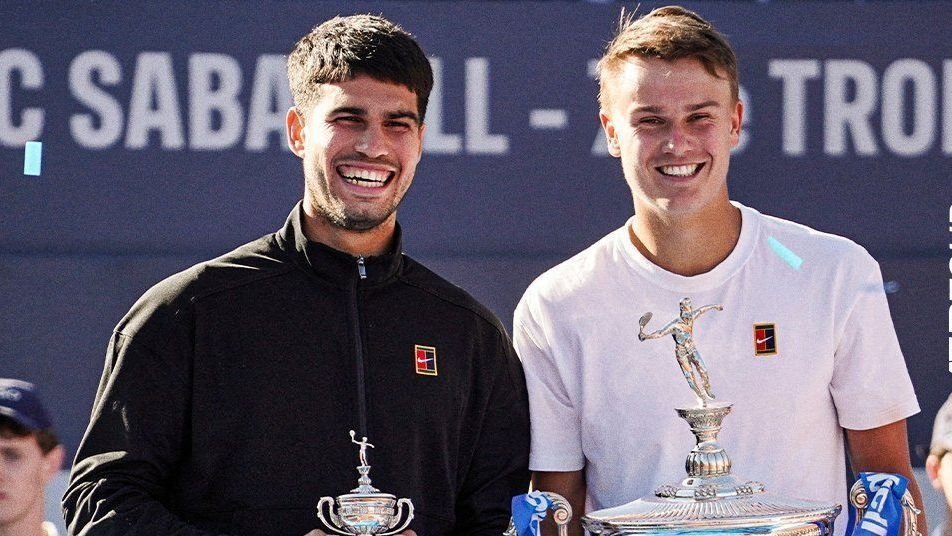 Alcaraz celebra amizade com Rune: desde os 12 anos nos courts 31 Dois jogadores de tênis sorrindo e segurando troféus, destacando conquistas no torneio ATP de Barcelona.