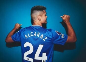 Jogador de futebol com camisa azul número 24, exibe o nome nas costas, em fundo azul, destacando o uniforme do time.