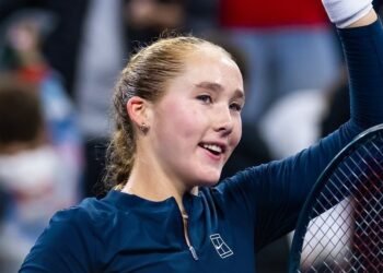 Andreeva, 17, vence irmã e avança em torneio de tênis 35 Jovem tenista sorridente levanta uma raquete de tênis, celebrando uma vitória em quadra durante um torneio.