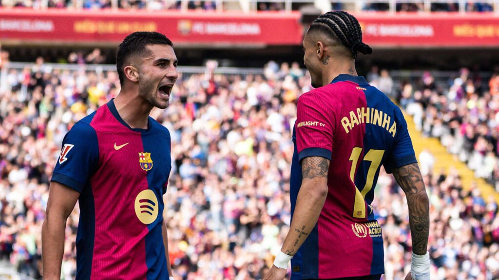 Jogadores do Barcelona celebram um gol em campo, rodeados por torcedores no estádio vibrante e lotado.