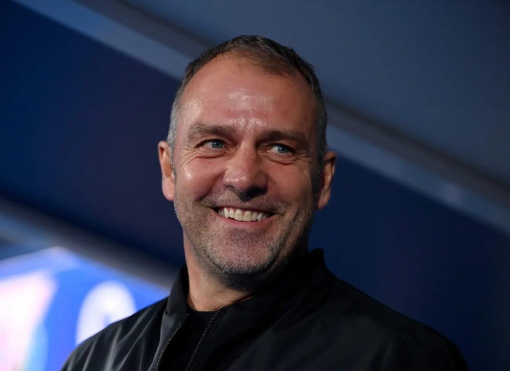 Homem sorridente com jaqueta preta em fundo desfocado, em ambiente iluminado, transmitindo confiança e simpatia.