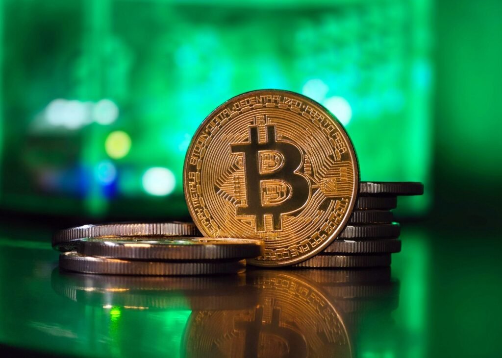 Moeda de Bitcoin dourada destacada sobre outras moedas em fundo verde, simbolizando o mercado de criptomoedas.