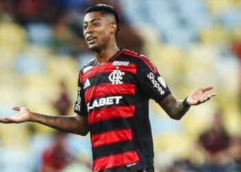 Jogador de futebol do Flamengo, em campo, gesticulando durante uma partida no estádio, vestindo uniforme rubro-negro.