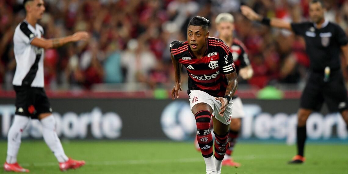 Jogador do Flamengo em ação durante partida, vestindo uniforme com listras vermelhas e pretas, corre pelo campo atento ao jogo.
