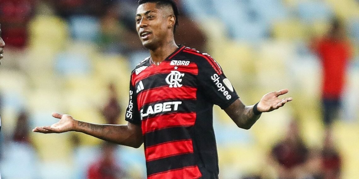 Jogador do Flamengo em campo, com expressão de dúvida, vestindo uniforme rubro-negro, em estádio iluminado.