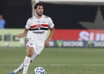 Calleri opera com sucesso; São Paulo revela novo status do atacante 35 Jogador de futebol do São Paulo conduz a bola em campo durante partida, vestindo uniforme branco com detalhes vermelhos e pretos.