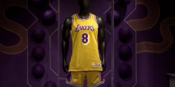 Uniforme amarelo dos Lakers com número 8 em manequim, exibido em cenário temático de basquete com bolas roxas decorativas.