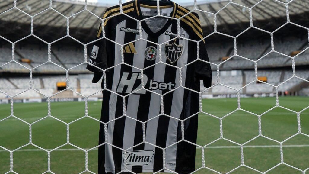 Camisa do Atlético Mineiro pendurada em uma rede de gol no estádio vazio, destacando listras preto e branco.