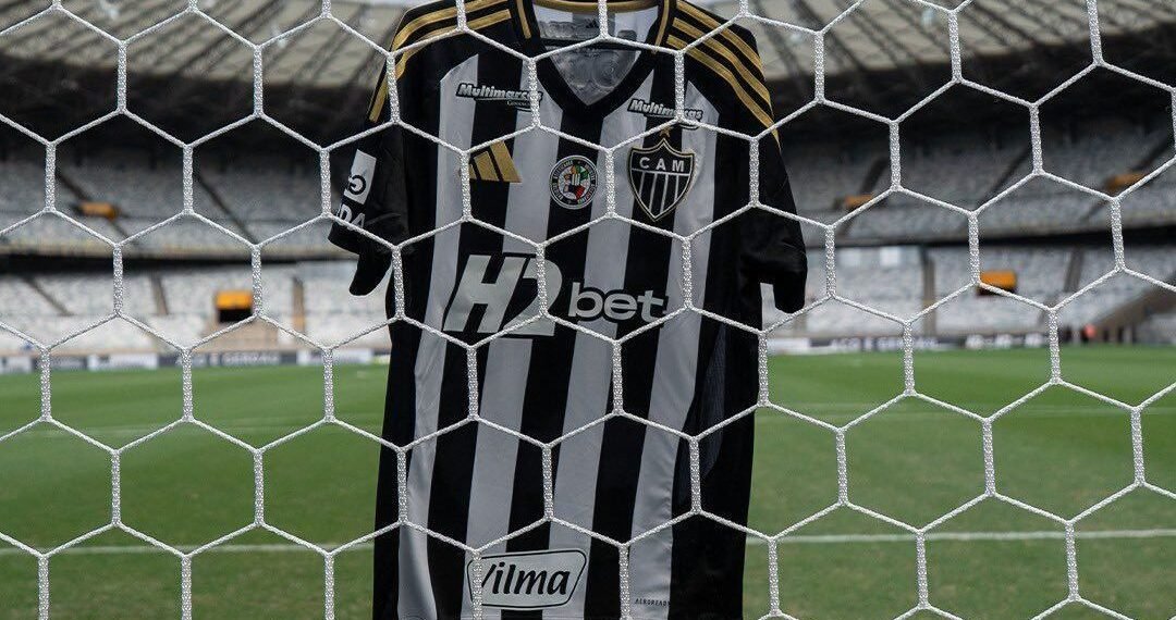 Camisa do Atlético Mineiro pendurada em uma rede de gol no estádio vazio, destacando listras preto e branco.