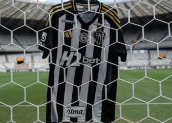 Camisa do Atlético Mineiro pendurada em uma rede de gol no estádio vazio, destacando listras preto e branco.