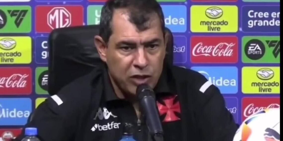 Treinador do Vasco dá entrevista coletiva após o jogo, com patrocinadores ao fundo, abordando temas esportivos.