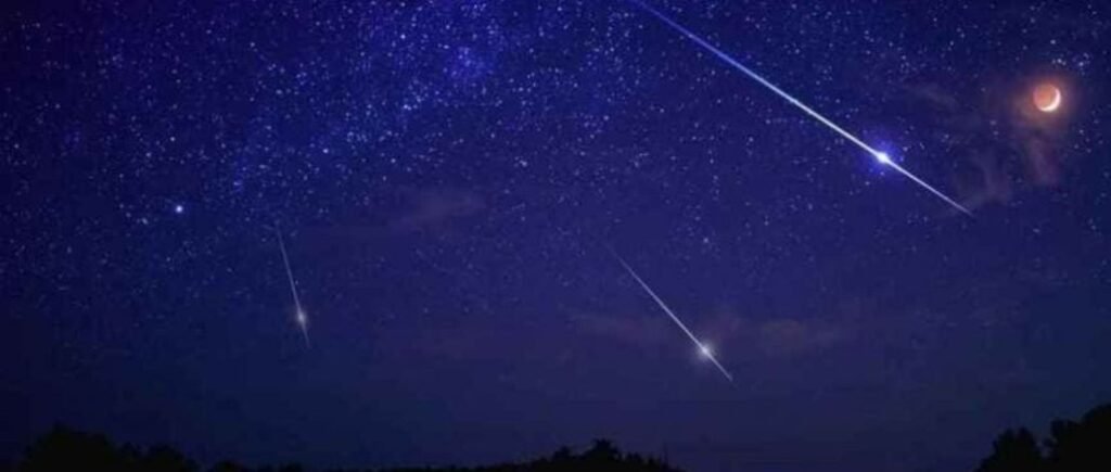 Céu estrelado à noite com meteoro riscando o horizonte e lua crescente ao fundo, ideal para observar fenômenos astronômicos.