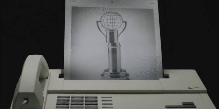 Um aparelho de fax antigo imprimindo a imagem de um troféu estilizado com globo no topo, destacando tecnologia retro.