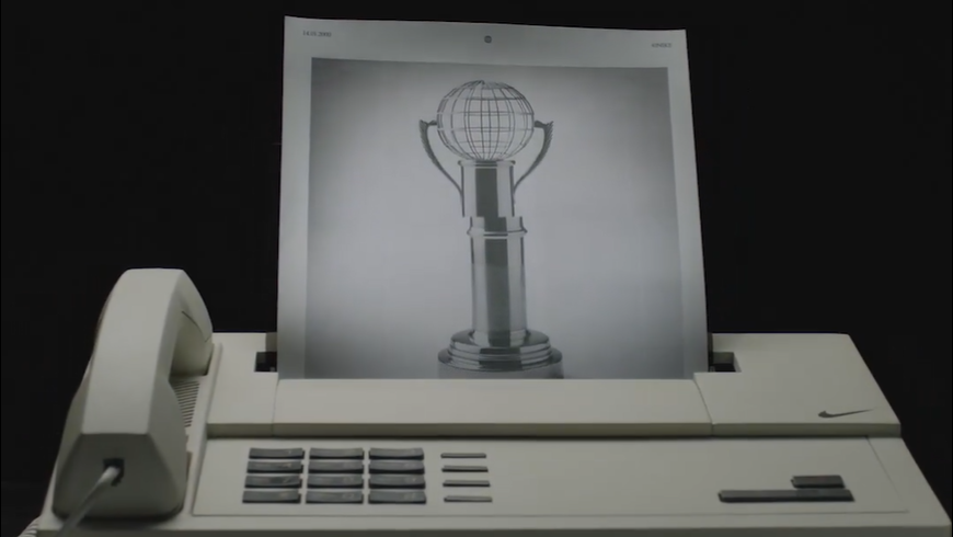 Um aparelho de fax antigo imprimindo a imagem de um troféu estilizado com globo no topo, destacando tecnologia retro.