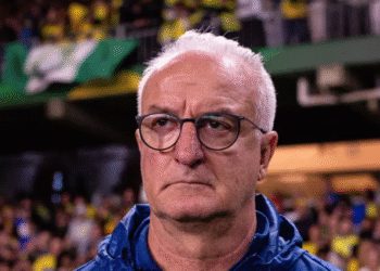 Corinthians avança nas negociações para contratar Dorival 39 Homem de óculos com expressão séria observa uma partida de futebol em estádio lotado, bandeiras e fãs ao fundo.