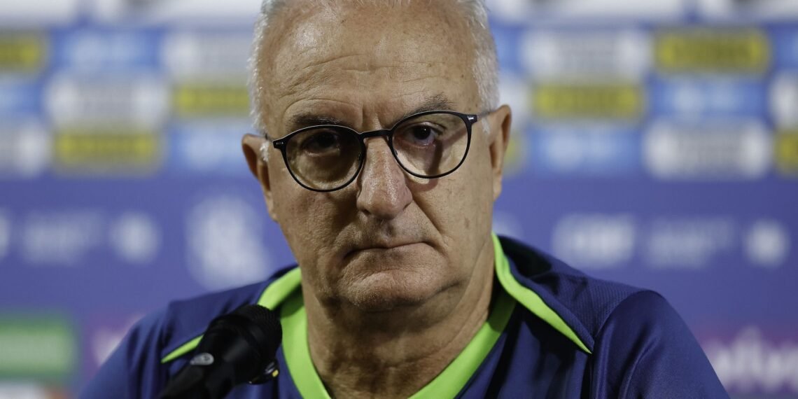 Homem de óculos em coletiva de imprensa, com fundo de logomarcas esportivas, aparenta concentração e seriedade.