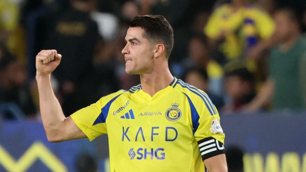 Jogador de futebol com uniforme amarelo e azul comemora com punho cerrado em partida, demonstrando determinação no campo.