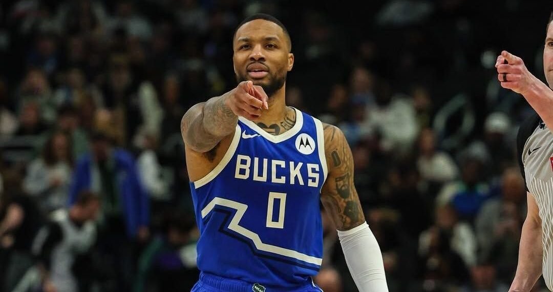 Jogador de basquete do Milwaukee Bucks em quadra, usando uniforme azul, aponta, concentrado durante o jogo.