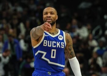 Jogador de basquete do Milwaukee Bucks em quadra, usando uniforme azul, aponta, concentrado durante o jogo.
