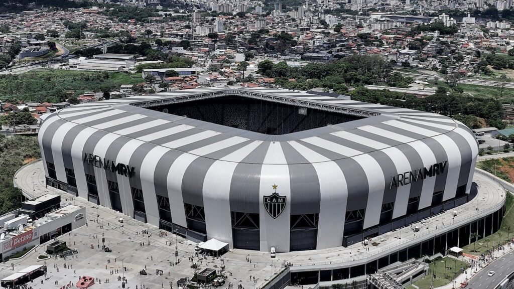 Vista aérea da Arena MRV, estádio moderno em formato retangular, cercado por áreas urbanas e movimento de pessoas.