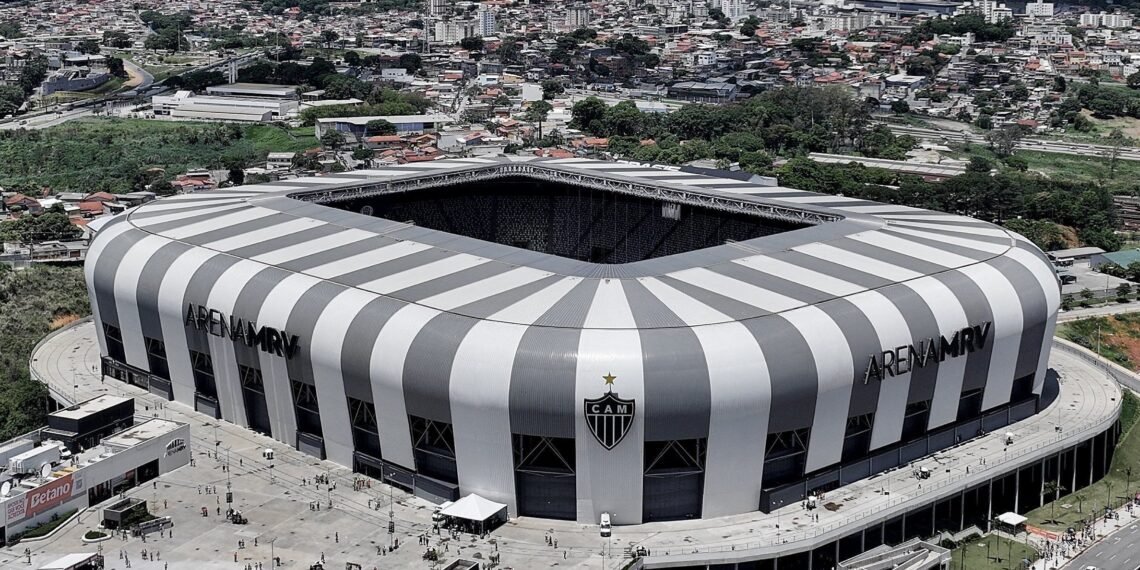 Vista aérea da Arena MRV, estádio moderno em formato retangular, cercado por áreas urbanas e movimento de pessoas.