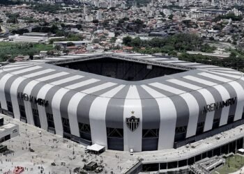 Vista aérea da Arena MRV, estádio moderno em formato retangular, cercado por áreas urbanas e movimento de pessoas.
