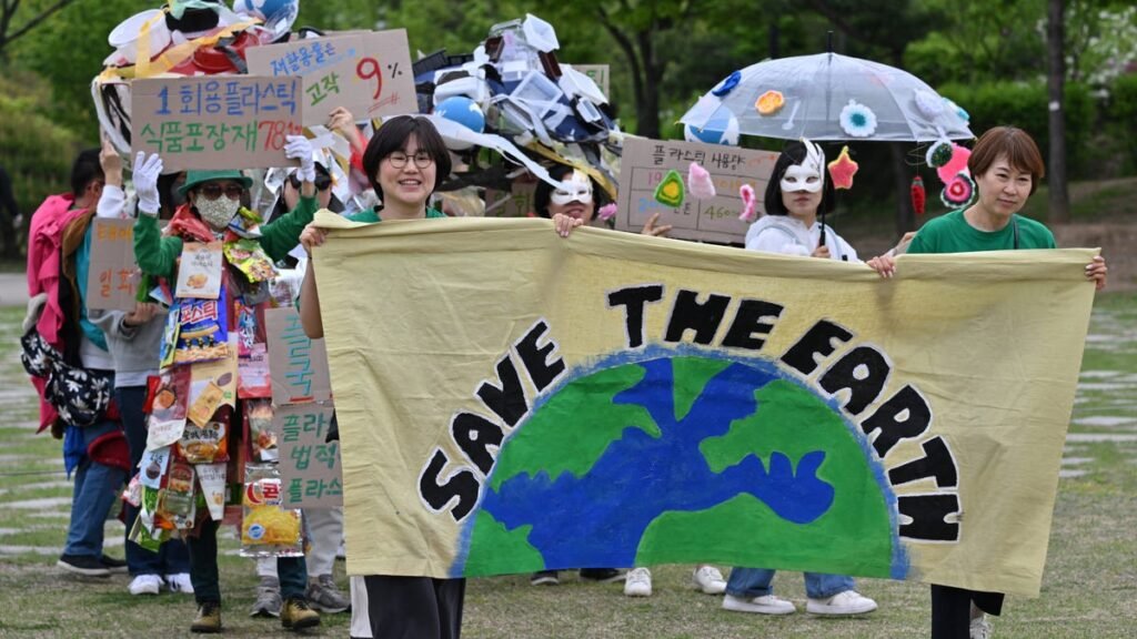 Grupo de pessoas em marcha ambiental segura faixa Save the Earth e cartazes sobre reciclagem e poluição plástica.