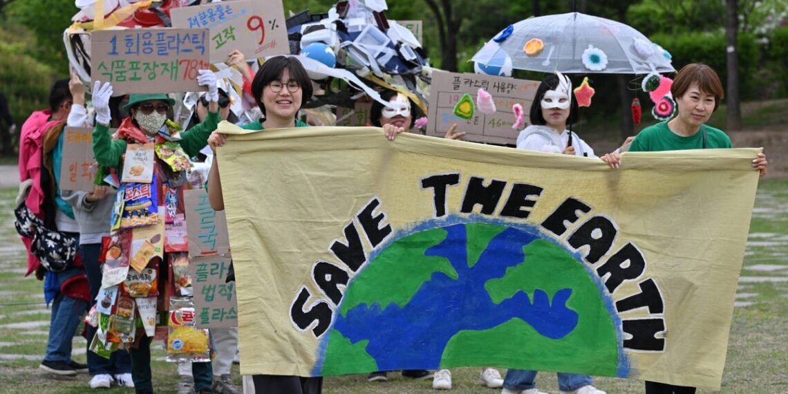 Grupo de pessoas em marcha ambiental segura faixa Save the Earth e cartazes sobre reciclagem e poluição plástica.
