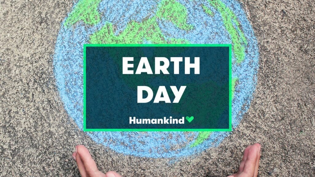 Desenho de giz no chão com um planeta Terra e mãos ao redor, destacando a mensagem Earth Day e Humankind.