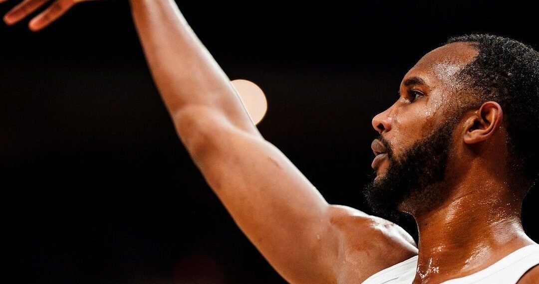 Jogador de basquete arremessando bola em quadra, destacando foco e intensidade do movimento esportivo.