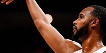 Jogador de basquete arremessando bola em quadra, destacando foco e intensidade do movimento esportivo.