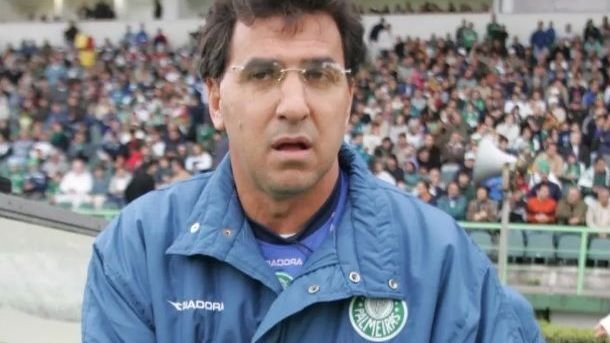 Homem usando jaqueta do Palmeiras em estádio lotado, cercado por torcida, aparenta estar concentrado no ambiente esportivo.