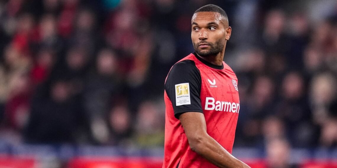 Jogador de futebol do Bayer Leverkusen em campo, vestindo uniforme vermelho e preto, durante uma partida na Bundesliga.