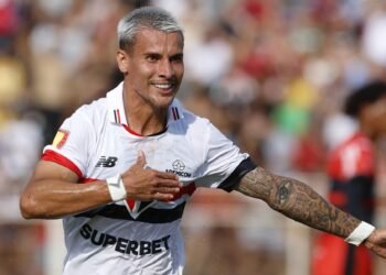 Ferreirinha, do São Paulo, responde aposta de Neto: “Contagem regressiva” 33 Jogador de futebol comemorando gol, exaltando emoção em campo, com uniforme branco e tatuagens visíveis no braço.