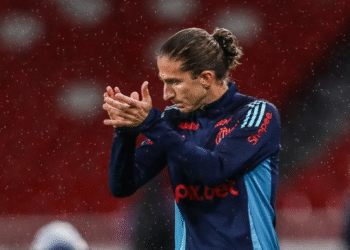 Filipe Luís apoia jogadores do Flamengo após críticas de torcedores 38 Jogador de futebol com uniforme azul escuro aplaude sob chuva em estádio, destacando empenho e resistência no esporte.