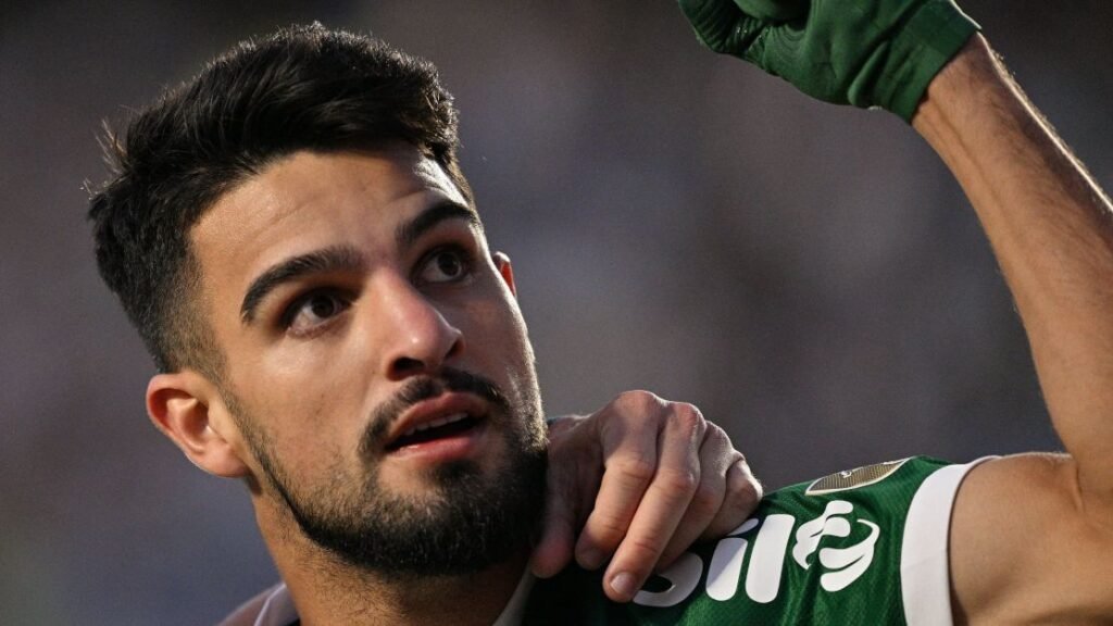 Jogador de futebol do Palmeiras celebra com expressão confiante, levantando o braço, em campo durante partida.