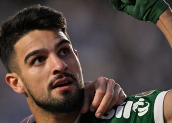 Jogador de futebol do Palmeiras celebra com expressão confiante, levantando o braço, em campo durante partida.