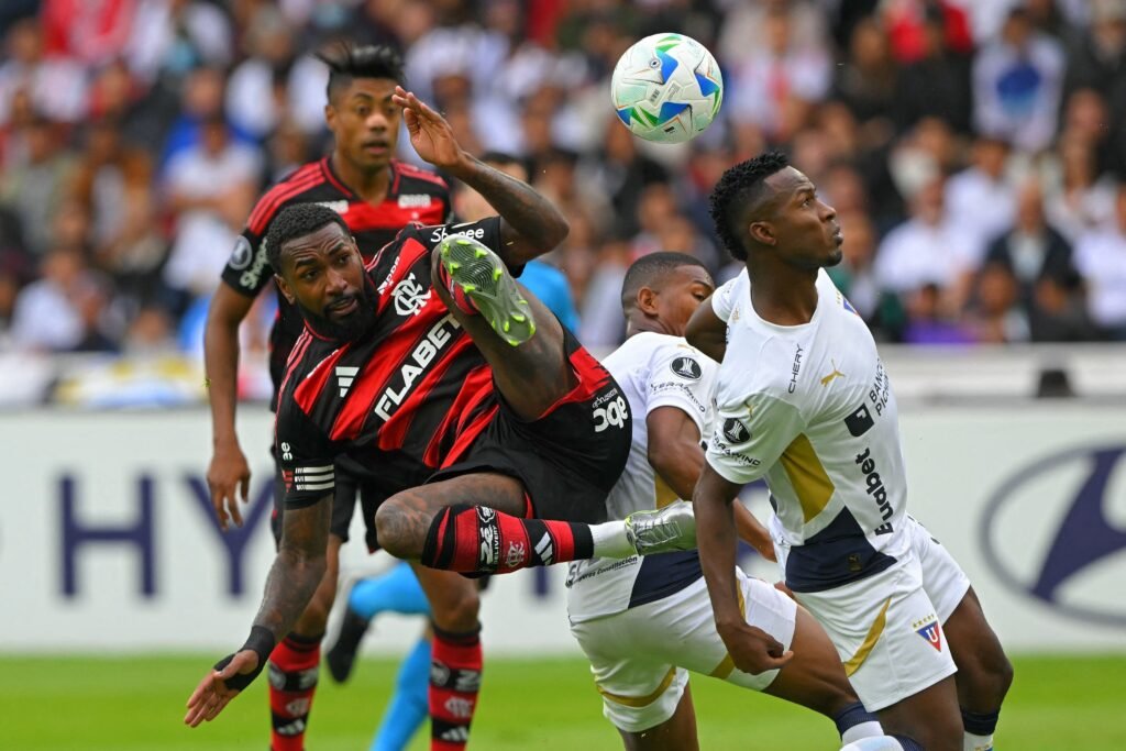 Jogador do Flamengo realiza bicicleta em campo disputando bola com adversários durante partida de futebol movimentada.
