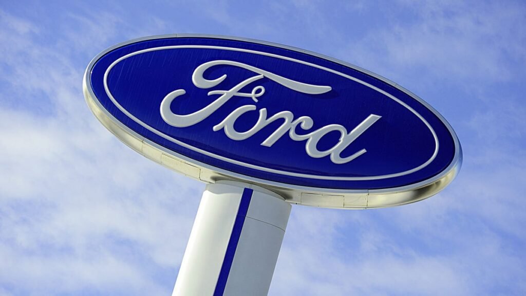 Logotipo da Ford em fundo azul e branco, destacando a marca automotiva sob um céu azul claro com nuvens dispersas.