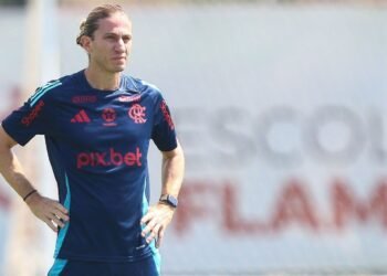 Gordura: O trunfo do Flamengo além do Brasileirão 40 Treinador de futebol com uniforme de treino azul do Flamengo observa o campo com as mãos na cintura, destacando concentração.