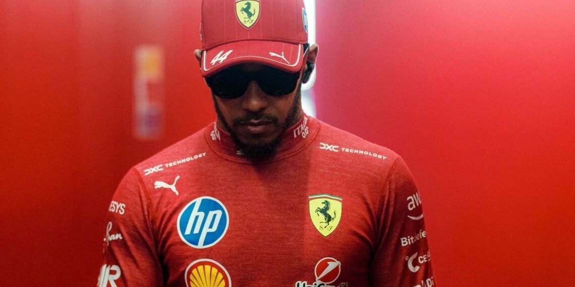 Piloto de Fórmula 1 veste uniforme vermelho da Ferrari com logotipos de patrocinadores, usando boné e óculos escuros.
