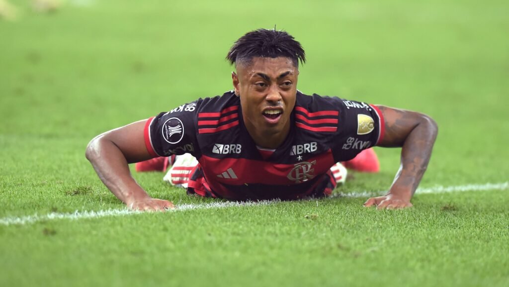 Jogador de futebol do Flamengo deitado no gramado durante partida, expressando determinação e esforço no jogo.