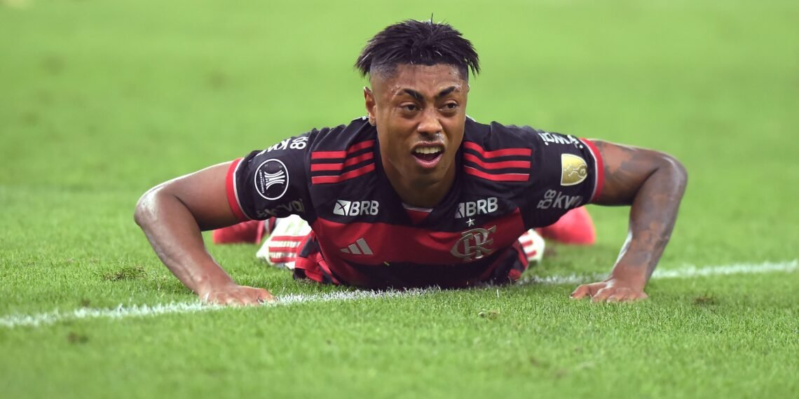 Jogador de futebol do Flamengo deitado no gramado durante partida, expressando determinação e esforço no jogo.