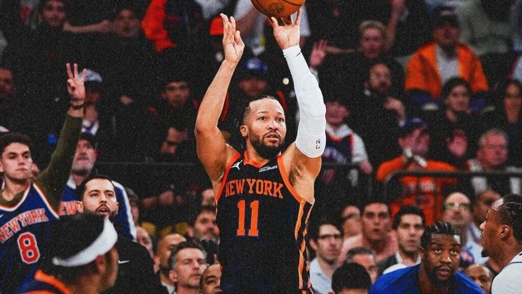Jogador do New York Knicks arremessa bola de basquete em quadra lotada, enquanto torcida observa atenta a jogada decisiva.