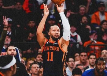 Jogador do New York Knicks arremessa bola de basquete em quadra lotada, enquanto torcida observa atenta a jogada decisiva.