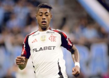 Jogador de futebol em ação com uniforme do Flamengo, durante partida em estádio, demonstrando concentração e agilidade.