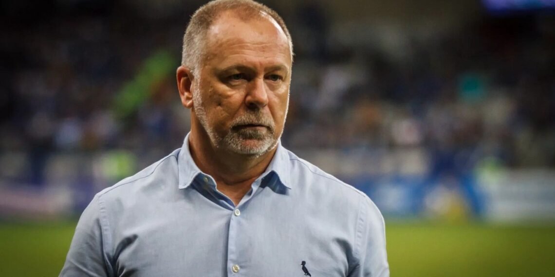 Homem de camisa azul claro observa atentamente um campo de futebol desfocado ao fundo, transmitindo foco e concentração.