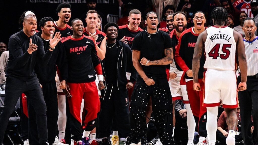 Jogadores de basquete celebram intensamente à beira da quadra, vestindo uniformes e roupas casuais, transmitindo entusiasmo.