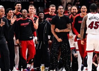 Miami Heat faz história: primeiro 10º a vencer no play-in! 32 Jogadores de basquete celebram intensamente à beira da quadra, vestindo uniformes e roupas casuais, transmitindo entusiasmo.